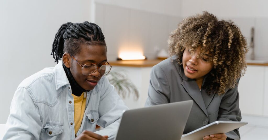 Two professionals discussing work on laptops and tablets in a modern office.